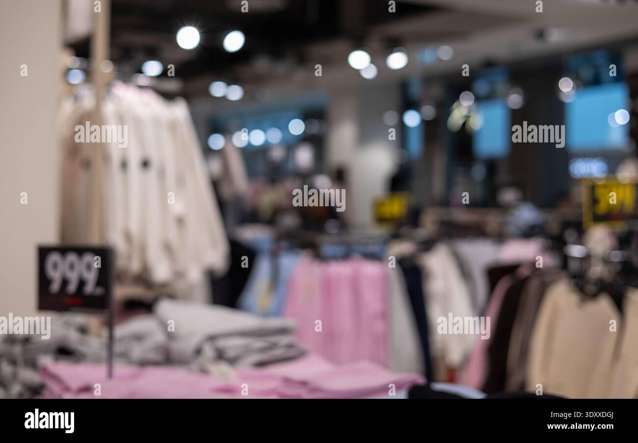 Verschwommenes Interieur eines modernen Modegeschäfts mit farbenfrohen Kleiderständern und Preisschildern mit sanfter Bokeh-Beleuchtung für einen Einkaufshintergrund Stockfoto
