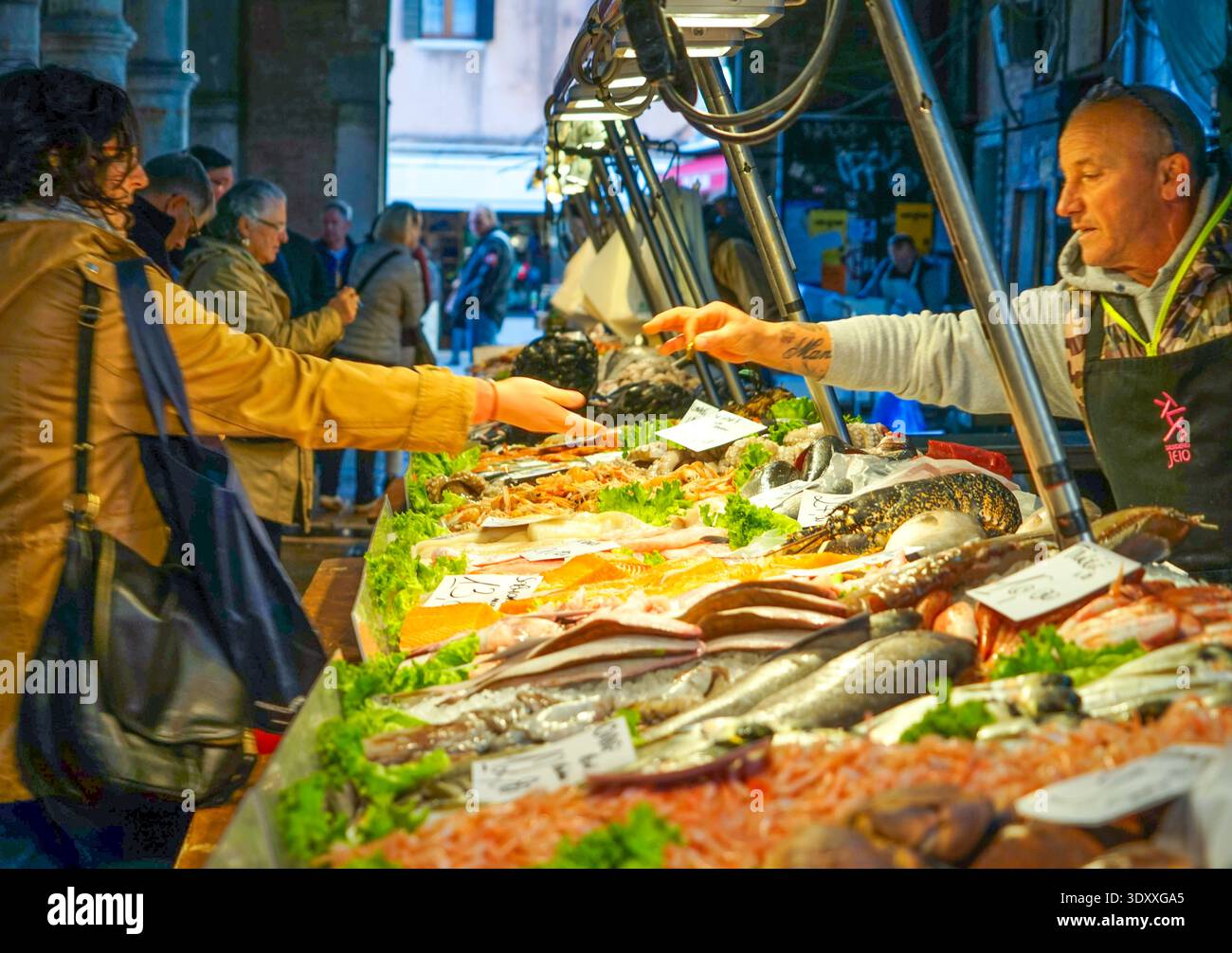 Fischhändler bedient einen Kunden mit frischen Meeresfrüchten auf dem Rialto-Fischmarkt in Venedig, Italien Stockfoto