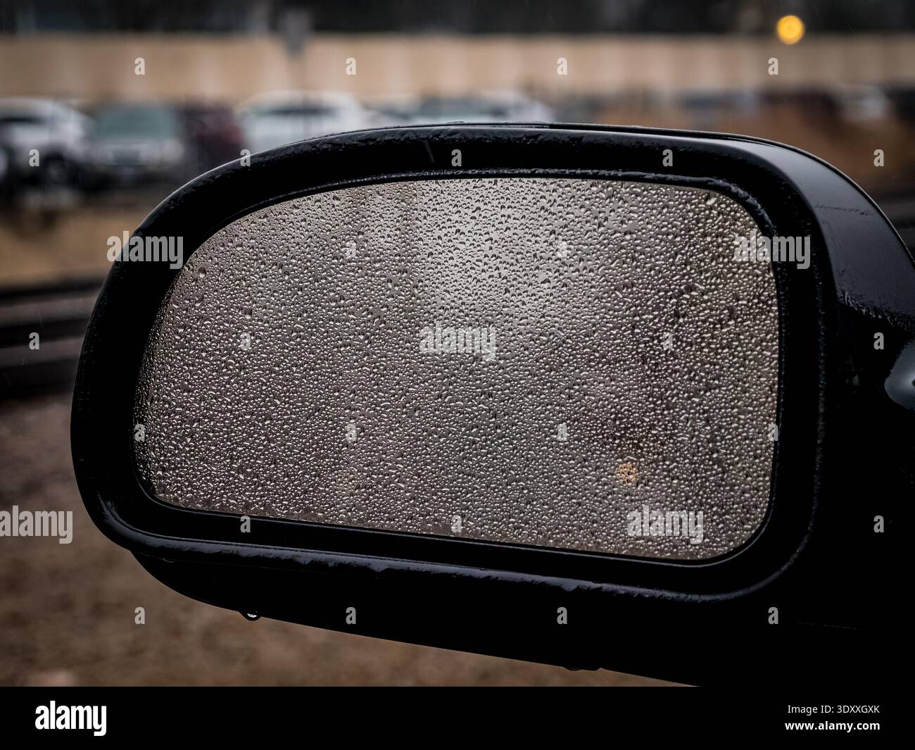 Nahaufnahme von Regentropfen auf einem Seitenspiegel des Autos mit verschwommenem Hintergrund an einem regnerischen Tag Stockfoto