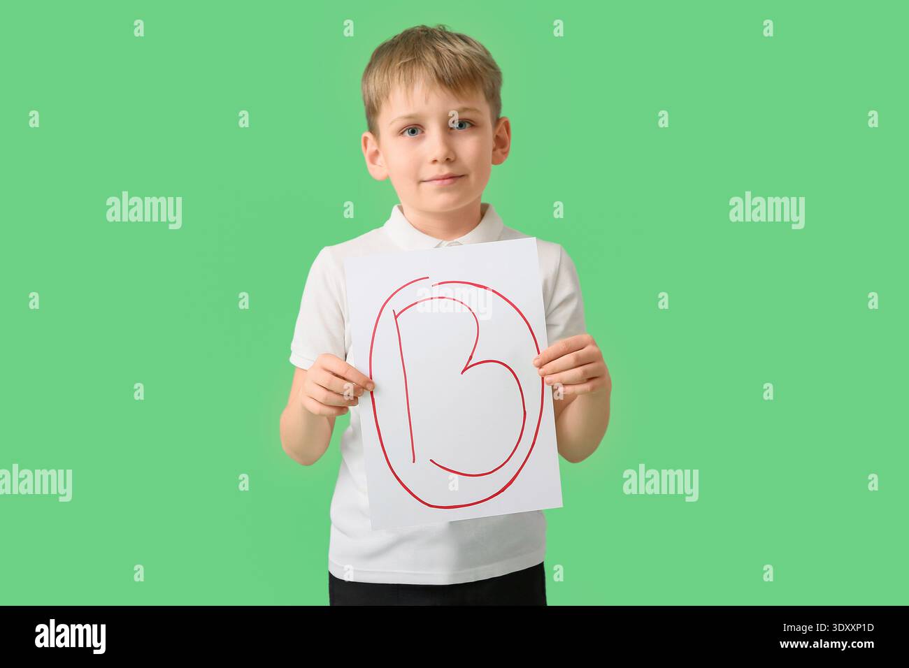 Glücklicher Schuljunge, der Papier mit guter Note auf grünem Hintergrund hält Stockfoto