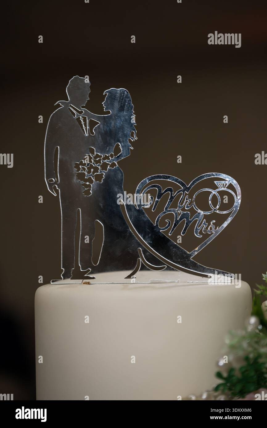 Eine lasergeschnittene Hochzeitstortenplatte aus Acryl mit silbernem Spiegel und einer Silhouette von Braut und Bräutigam und ineinander greifenden Ringen in einem Herzen. Stockfoto