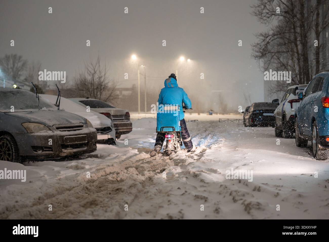 Transportkollaps in der Stadt bei Schneesturm, Lieferperson auf dem Fahrrad, die durch den Schnee läuft. Stockfoto
