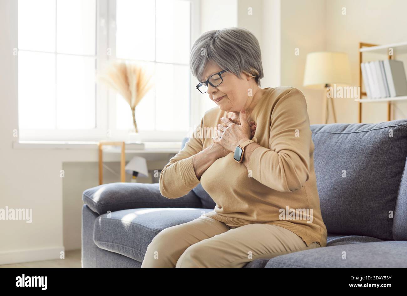 Ältere Frau mit Brustschmerzen, Herzinfarktsymptomen, auf Sofa sitzend Stockfoto