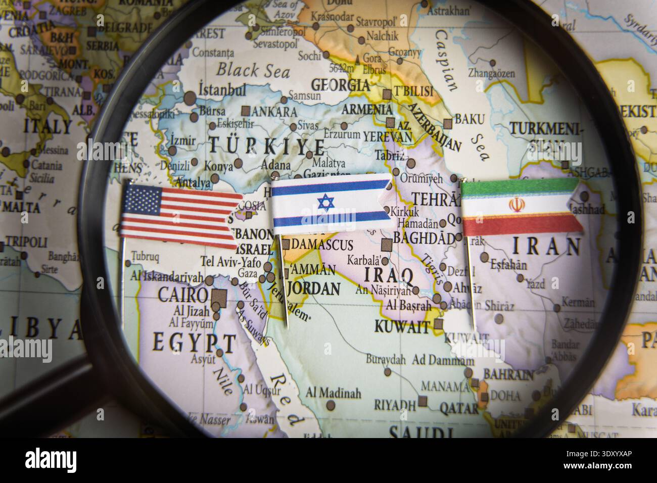 Vergrößerungsglas über einer geografischen Karte des Nahen Ostens mit Schwerpunkt auf den Flaggen der USA, Israels und Irans, Kriegskonzept, Konflikte, regionale Geopolitik Stockfoto