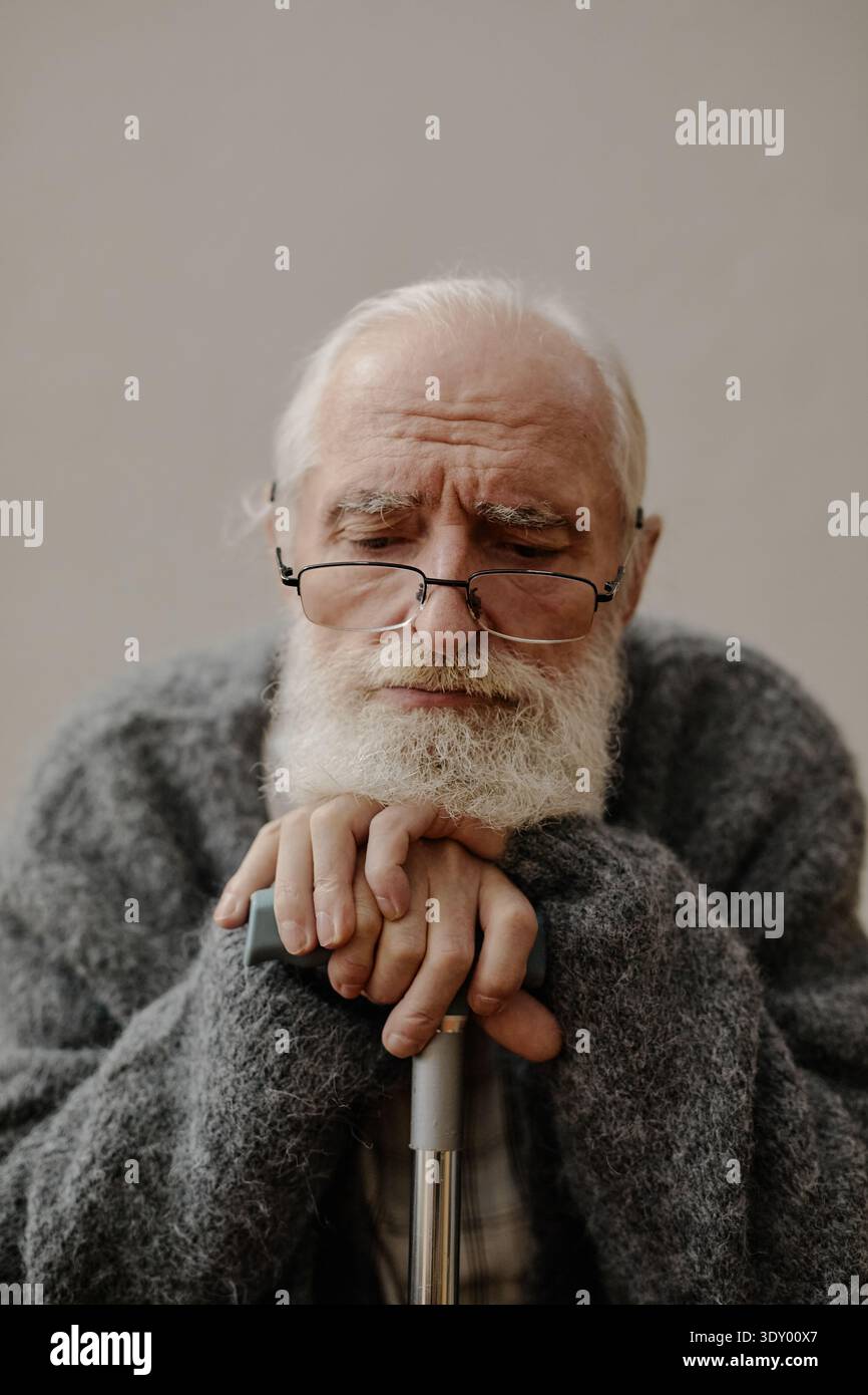Porträt eines älteren kaukasischen Mannes, der Hände auf Stock legt, während er drinnen sitzt Stockfoto
