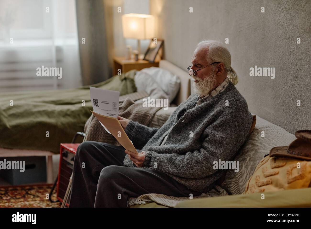 Senior-kaukasischer Mann sitzt drinnen und überprüft Rechnungen mit fokussiertem Ausdruck Stockfoto