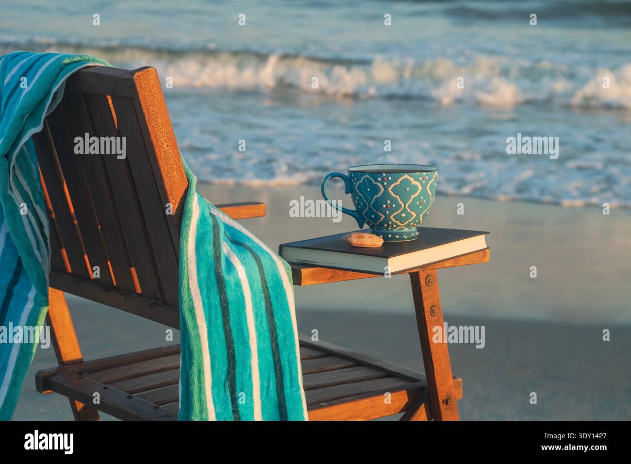 Antiker Strandstuhl vor dem Meer mit Handtuch, Boook und Kaffeetasse Stockfoto