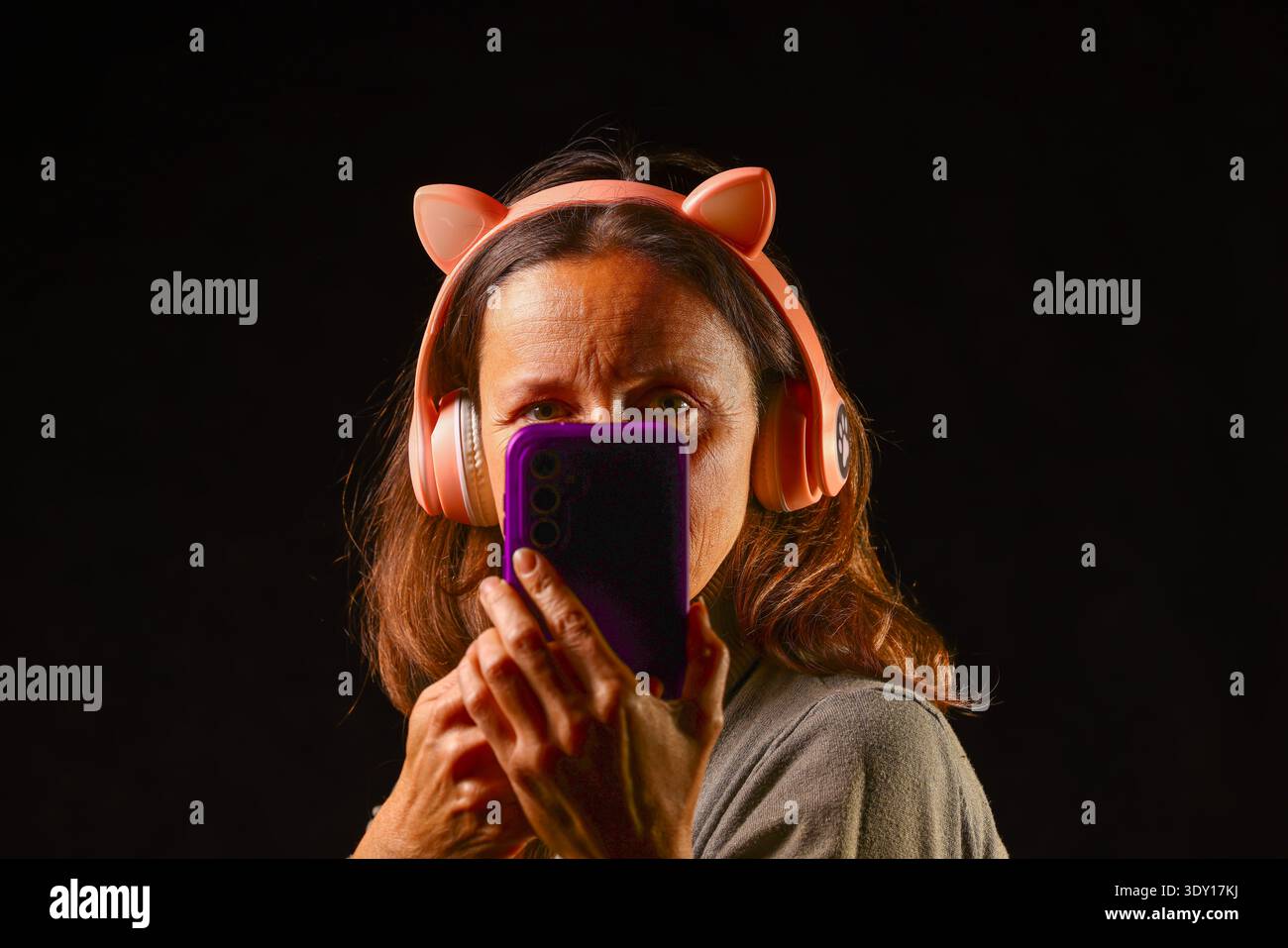 Frau, die vernetzte Audiotechnologie nutzt und verspielte Kopfhörer mit Smartphone-Steuerung für ein modernes digitales Musikerlebnis kombiniert Stockfoto