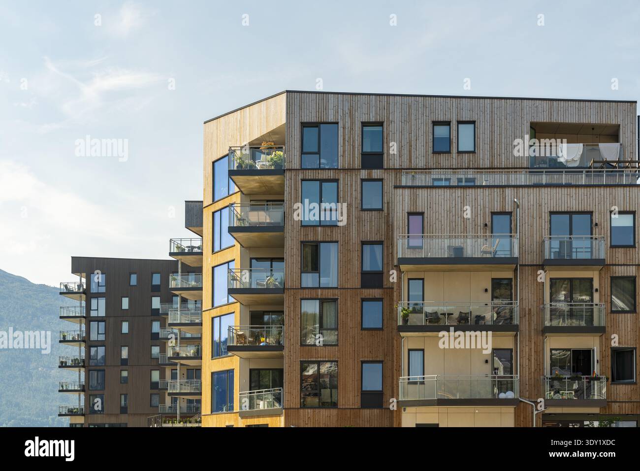 Blick auf moderne hölzerne Apartmenthäuser mit Glasbalkonen, die sich vor einem sanften blauen Himmel erheben, in einer malerischen Mischung aus urbaner und natürlicher Schönheit, Sogn Stockfoto