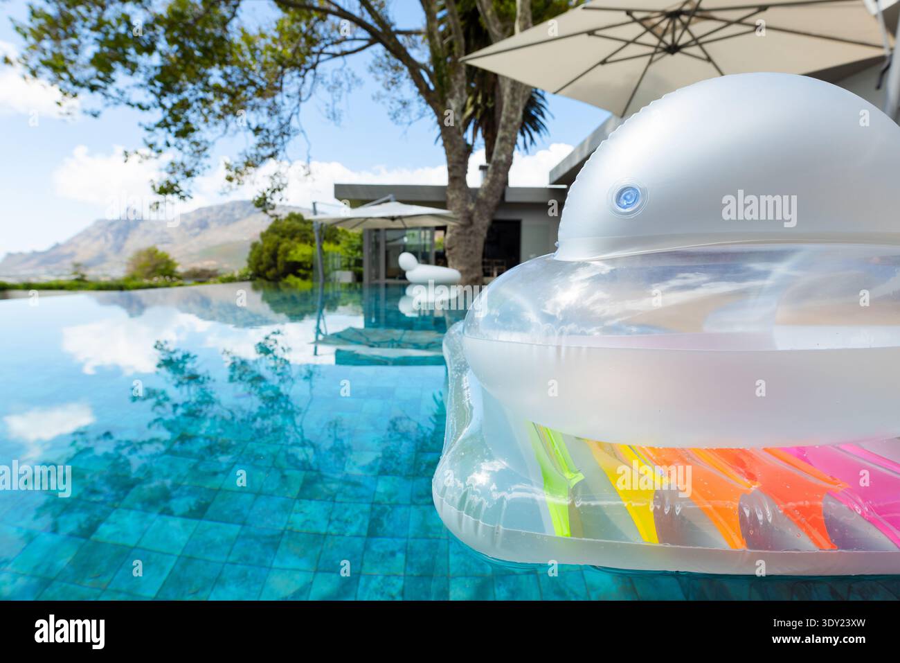 Durchscheinender aufblasbarer Schwimmer, der auf einem türkisfarbenen Infinity-Pool schwimmt und Himmel und Palmen reflektiert. Im Freien, Lounge, Terrasse, Villa, modern, minimalistisch Stockfoto