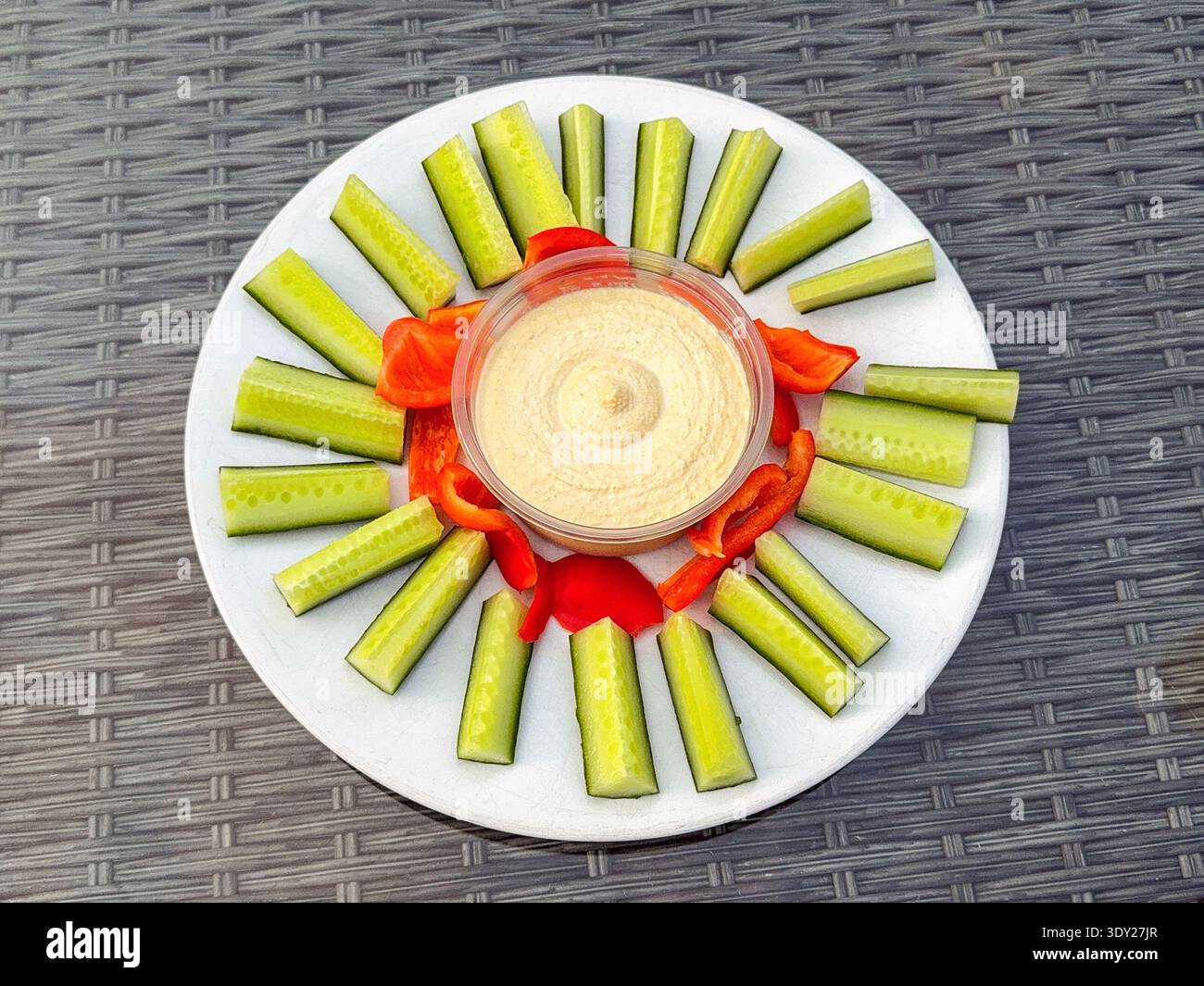 Gemüsesorten aus Gurke und rotem Pfeffer mit einer Schüssel Hummus Dip auf einem Gartentisch. Keine Personen. - Smartphone-aufgenommenes Stockfoto