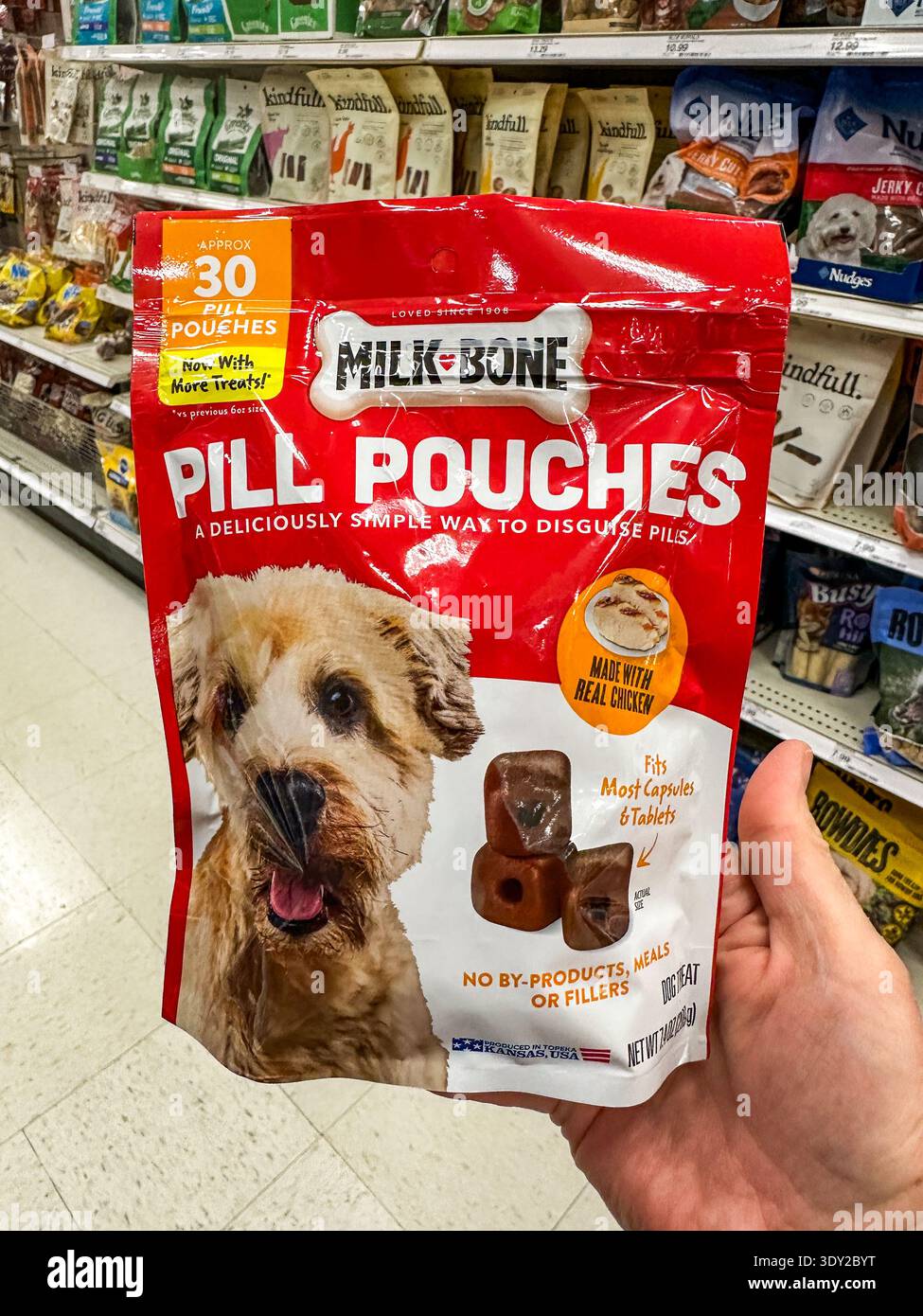 Eine Hand, die einen Sack mit Milchtummel für Hunde in einem Tiernahrungsgang in einem Markt hält - Smartphone-aufgenommenes Stockfoto