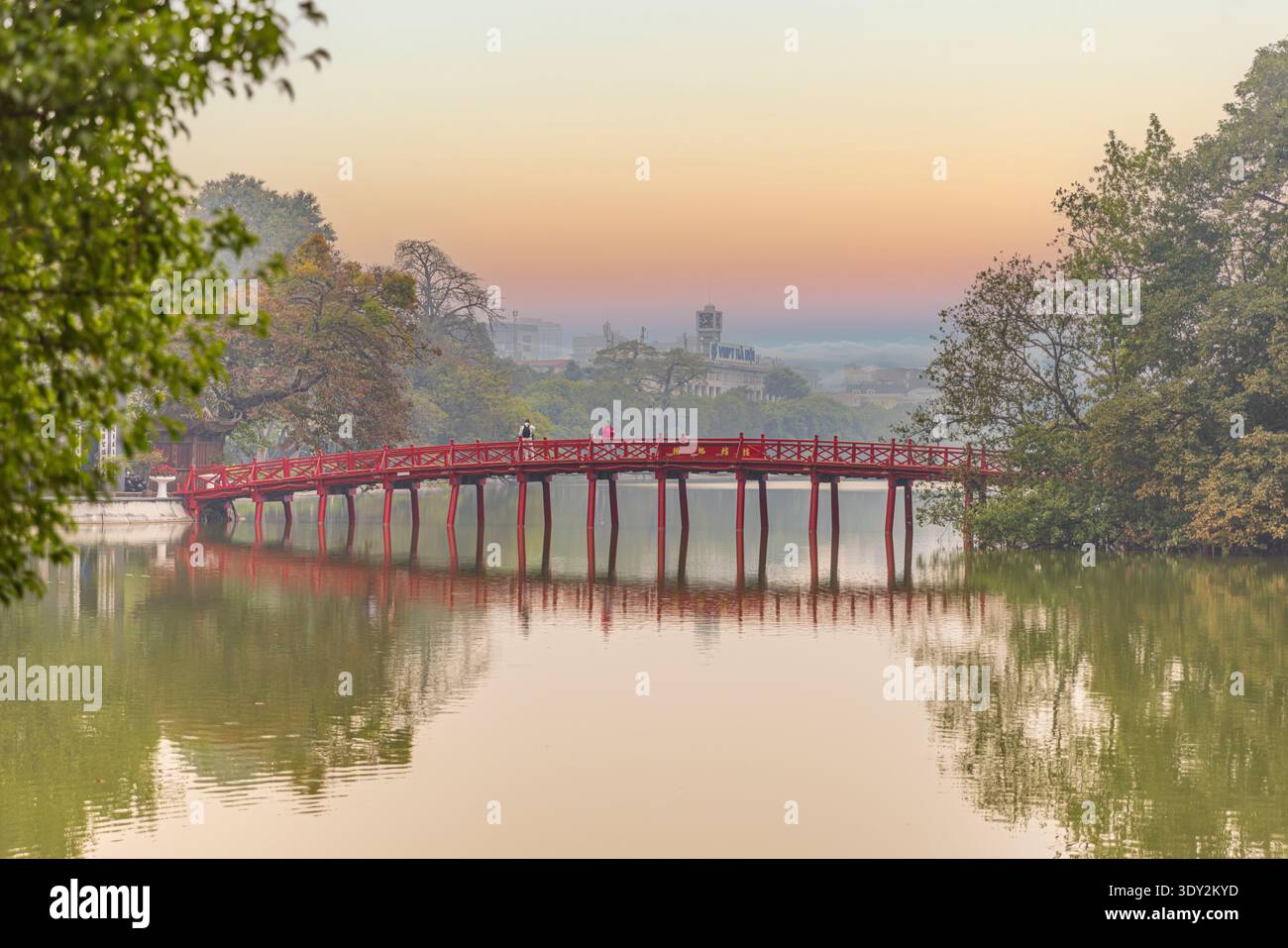 Die Huc-Brücke leuchtet rot im Licht eines orangen Sonnenuntergangs über dem Hoan Kiem-See in Hanoi. Stockfoto