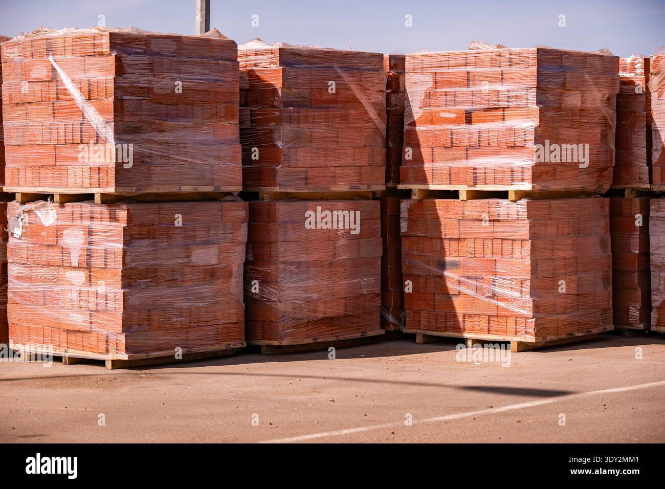 Stapel roter Ziegelsteine auf Holzpaletten, die für Bauzwecke mit Kunststofffolie abgedeckt sind Stockfoto