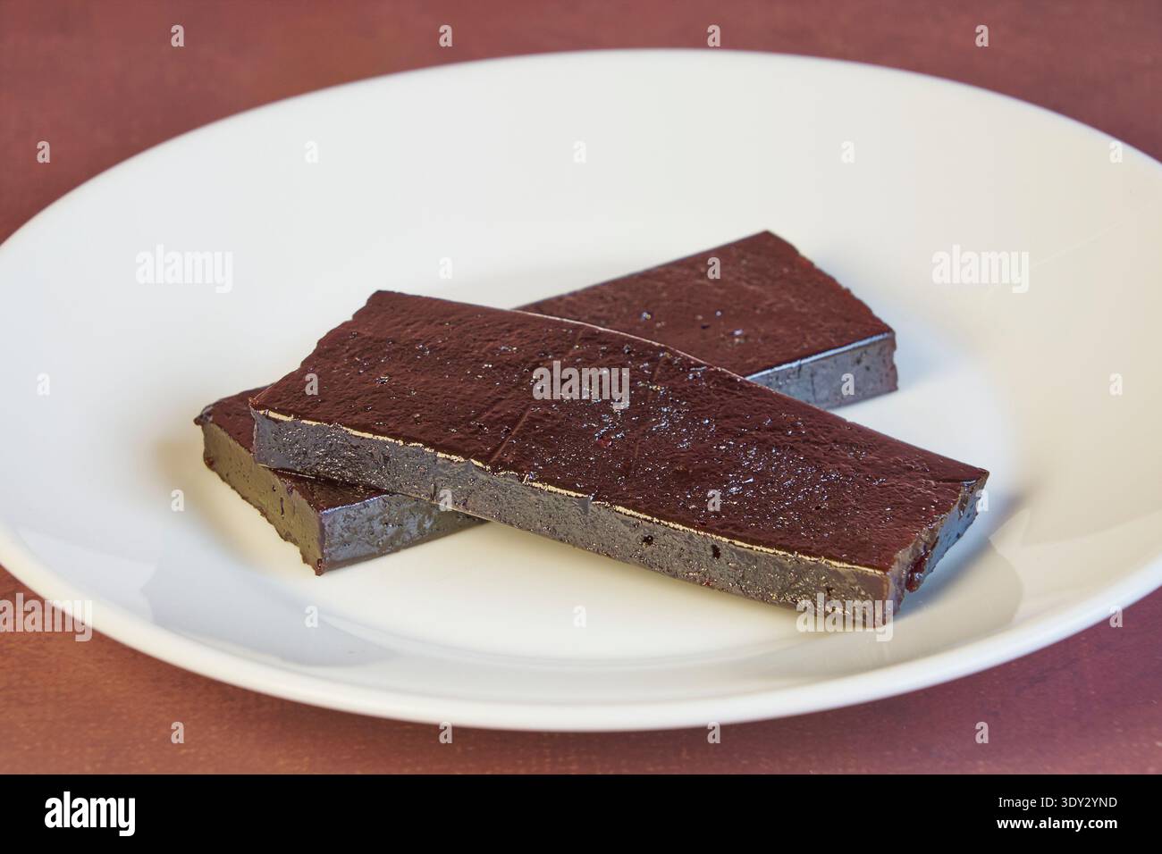 Dunkle Schokoladenriegel auf einer weißen Tafel, belegt mit Kakaopulver Stockfoto