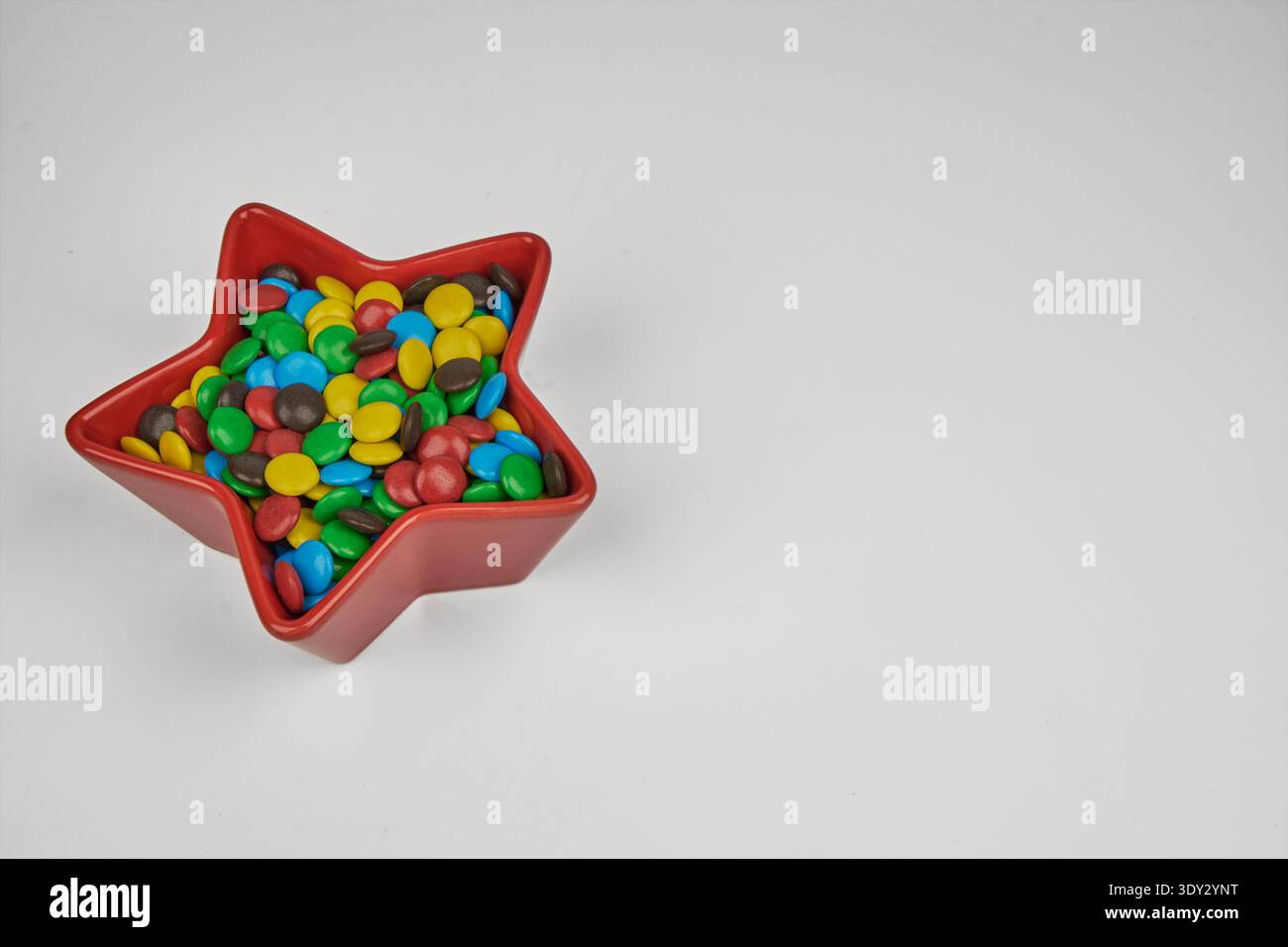 Bunte Schokoladenbonbons füllen eine rote sternförmige Schüssel auf einem sauberen weißen Hintergrund Stockfoto