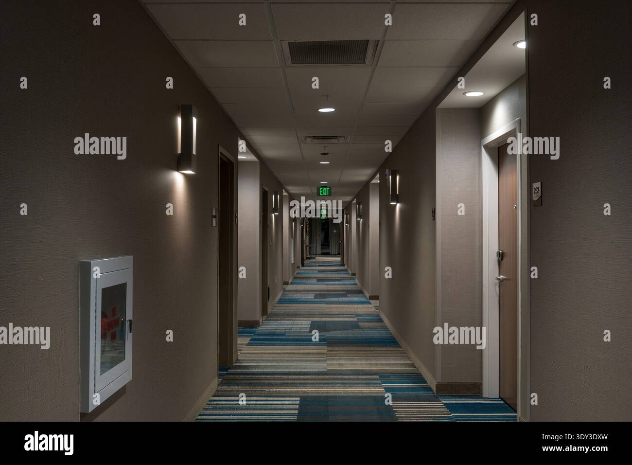 Langer Hotelflur mit Zimmertüren, Beleuchtung und Ausstiegsschildern. Stockfoto
