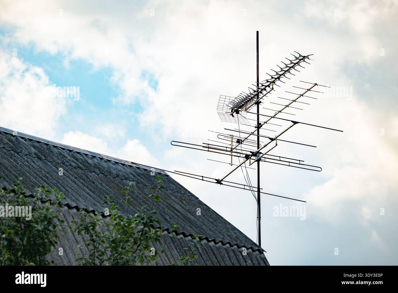 Alte Fernsehantenne auf dem Dach des Hauses, die mit dem Sendesignal am Himmel verbunden ist Stockfoto