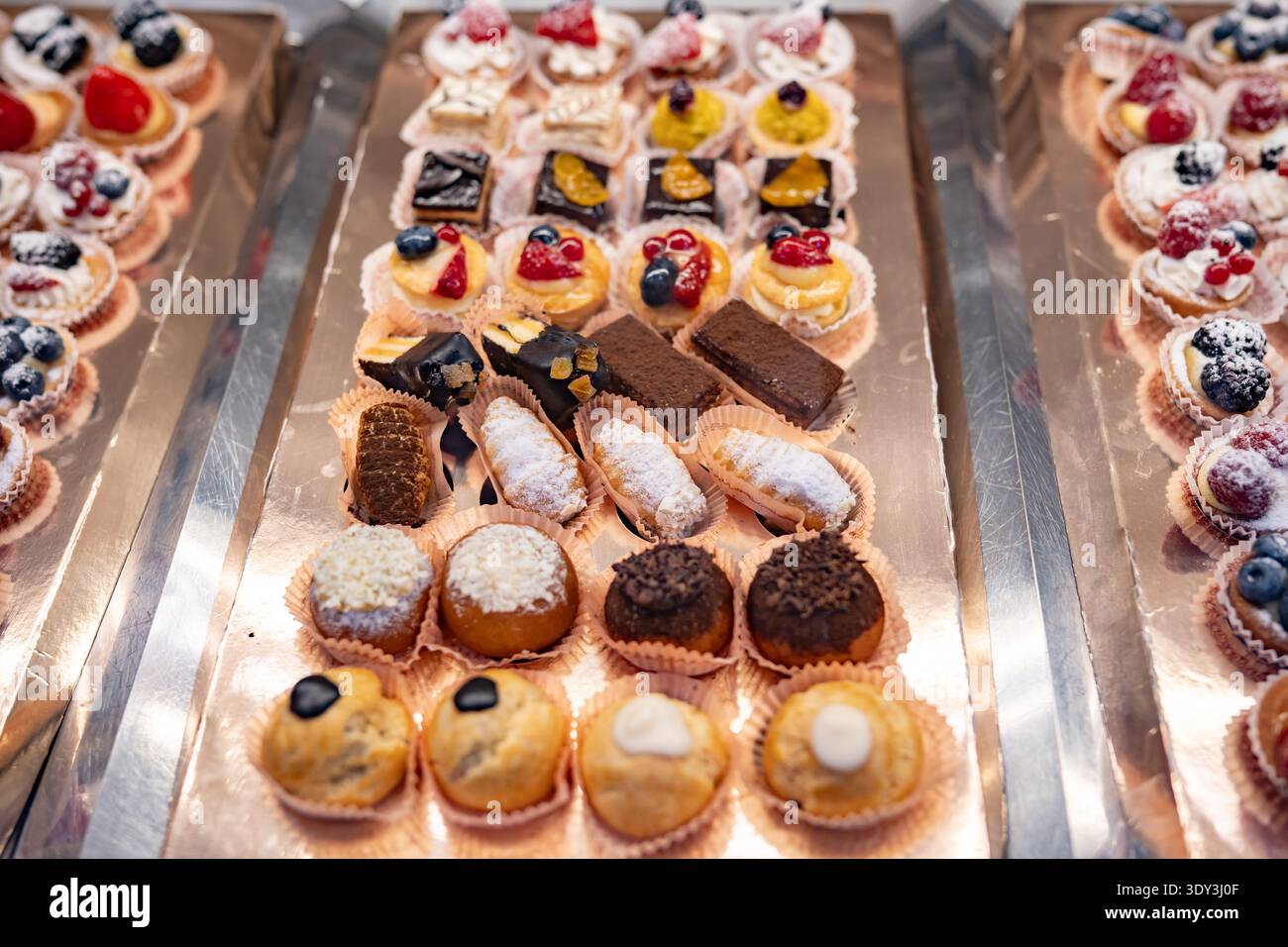 Auf silbernen Tabletts werden verschiedene köstliche Mini-Gebäckstücke, Kuchen und Obstkuchen präsentiert Stockfoto