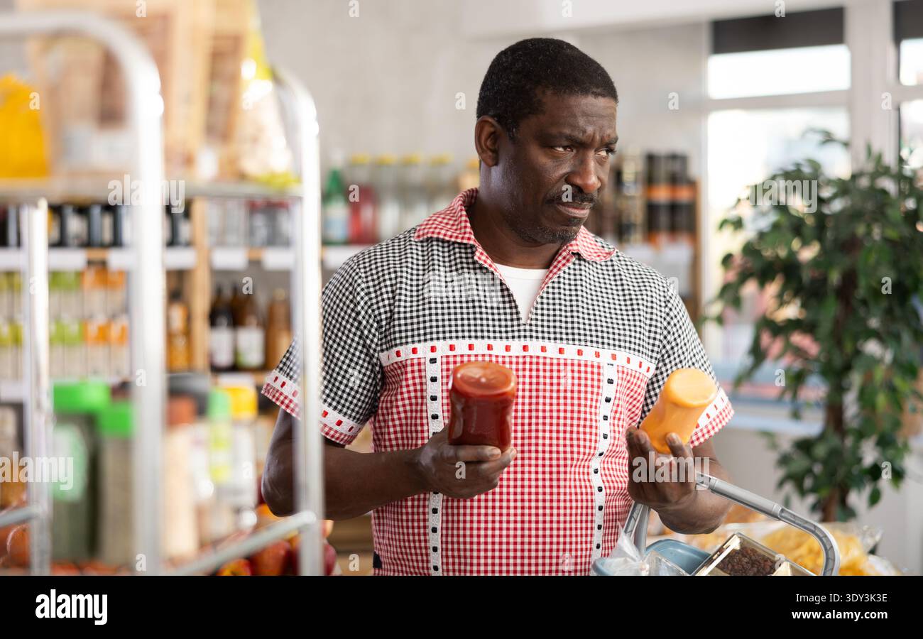 African man Buyer Select wählt mit Bedacht Flaschen mit verschiedenen Saucen aus Stockfoto