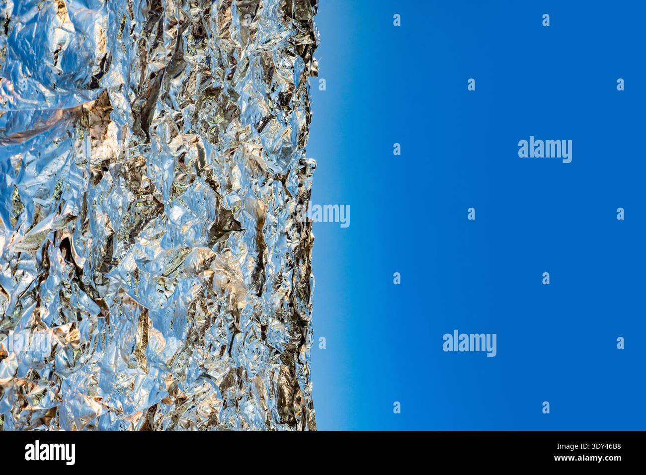 Zerknitterte Aluminiumfolie auf blauem Hintergrund, wodurch abstrakter Kopierraum entsteht Stockfoto