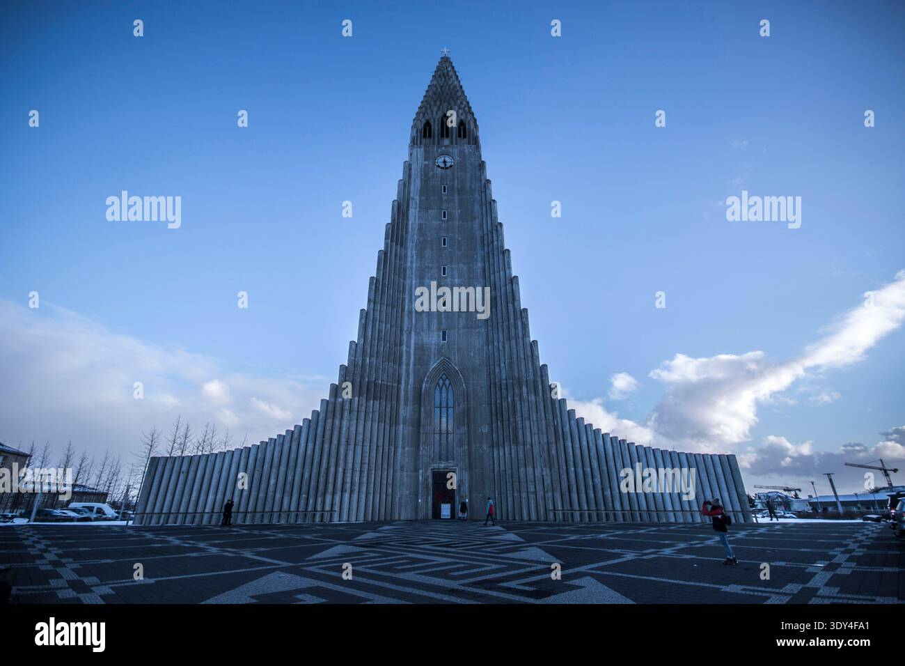 Die symmetrische Fassade der ikonischen Kirche Hallgrímskirkja in Reykjavik, Island, steht an einem sonnigen Wintertag hoch unter einem hellblauen Himmel. Stockfoto