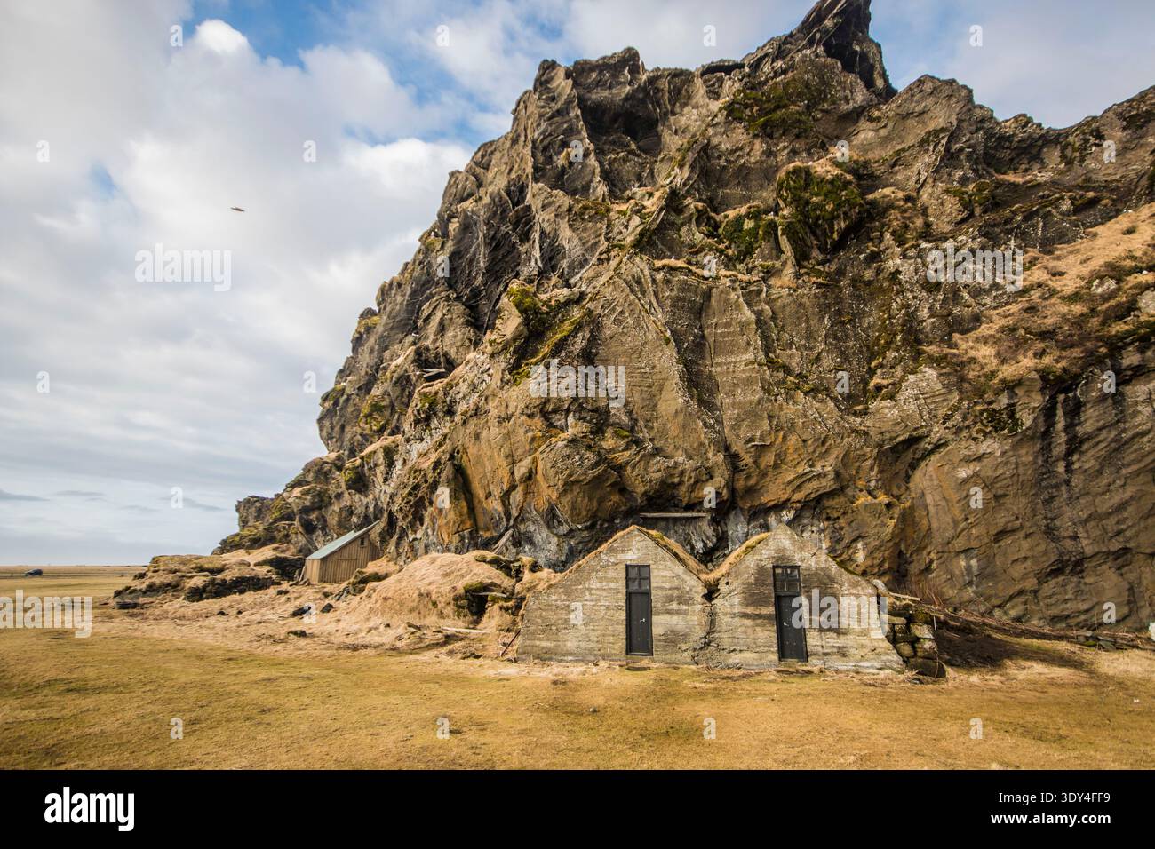 Historische Häuser mit Rasendach, die in den legendären Drangurinn-Felsen unter den Klippen von Drangshlíð, Südisland, eingebaut wurden. Stockfoto