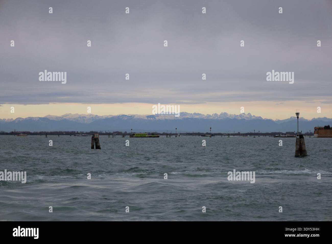Weite Aussicht über die Lagune von Venedig mit weit entfernten schneebedeckten Bergen unter dramatischen Wolken. Stockfoto