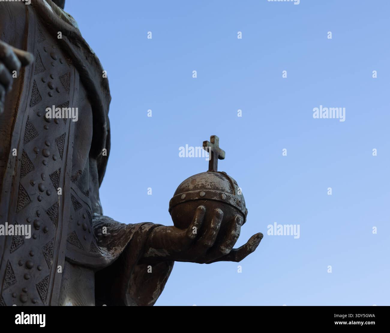 Nahaufnahme einer Bronzestatue mit einem Globus-Kreuzer, der königliche Macht und christentum symbolisiert, vor einem klaren blauen Himmel mit Polizisten Stockfoto
