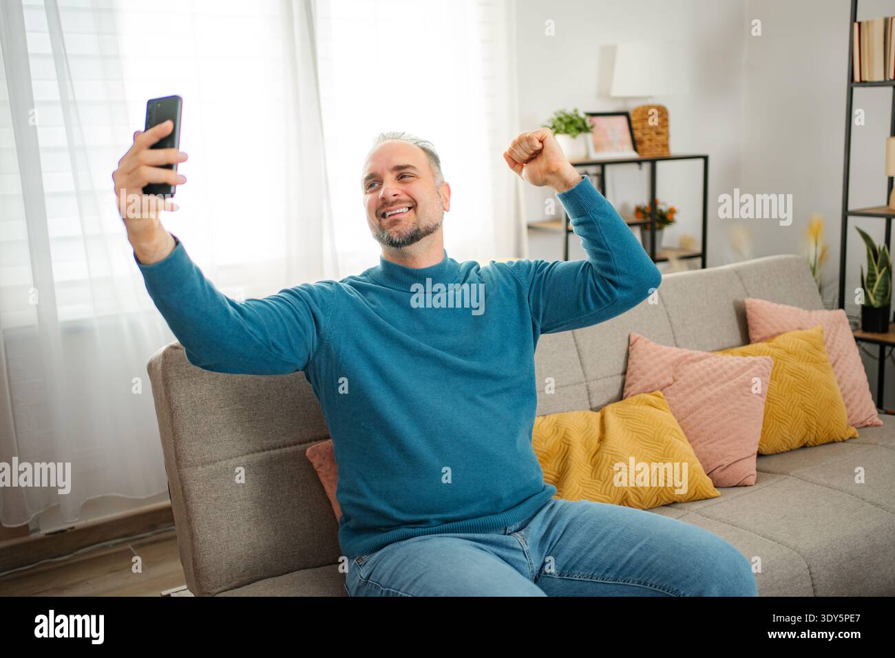 Glücklicher Mann, der zu Hause auf dem Handy den Sieg feiert Stockfoto