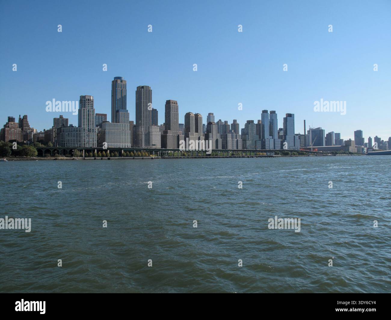 Ein Panoramablick auf Manhattan zeigt eine dichte Ansammlung von Hochhäusern, die sich hinter dem Fluss im Vordergrund erheben. Stockfoto