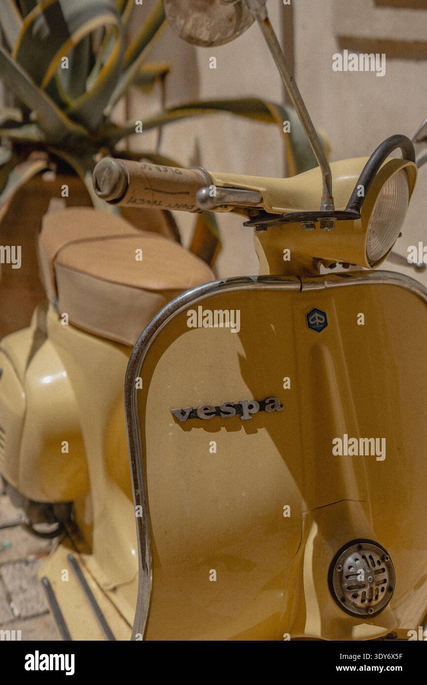 Gelbes Vespa-Moped, das in Korfu-Stadt mit Pflanzen und Gebäuden in der Nähe geparkt ist Stockfoto