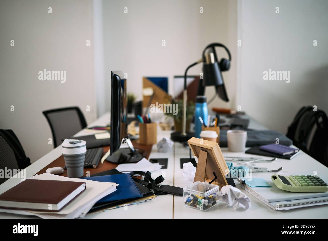 Unordentlicher Schreibtisch mit verstreuten Dokumenten, Kaffeetasse, Computermonitor, Taschenrechner, Schreibwaren, verwickelte Kabel und persönliche Gegenstände, die zur Reinigung und Organisation anstehen Stockfoto