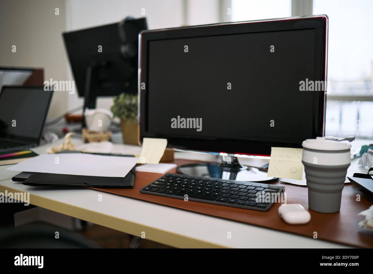 Leerer Bürotisch mit Computermonitor, Tastatur, kabelloser Maus, wiederverwendbarer Kaffeetasse, Ordnern, Haftnotizen und andere wichtige Arbeitsmaterialien, Arbeitsbereich scheint kürzlich bereinigt zu sein Stockfoto