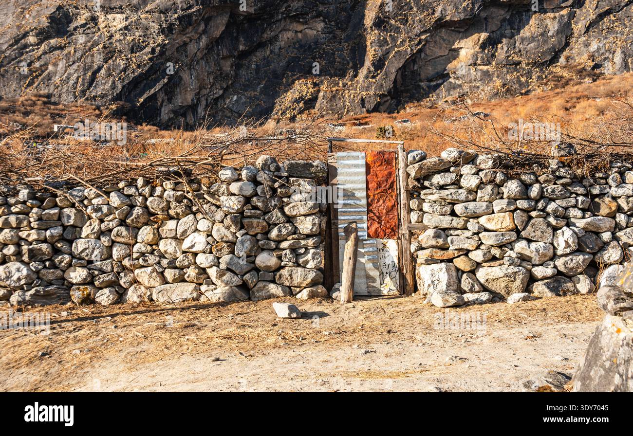 Steinmauer und Holztür mit sonnendurchfluteten Bergen im Langtang Valley, Nepal Stockfoto