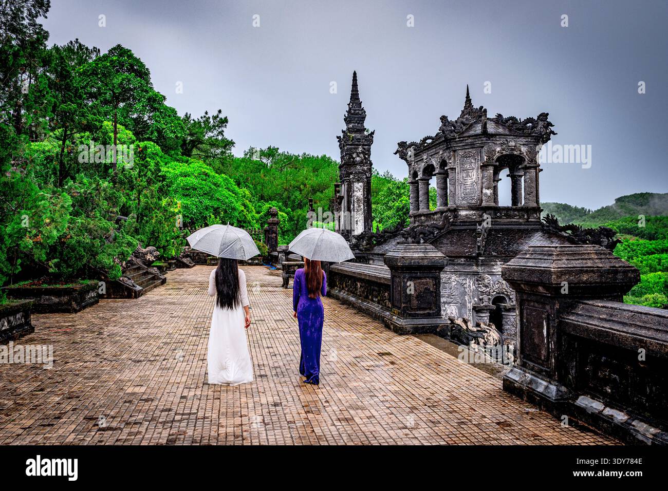 Frauen laufen mit Sonnenschirmen an einem historischen Ort in Vietnam bei bewölktem Wetter Stockfoto