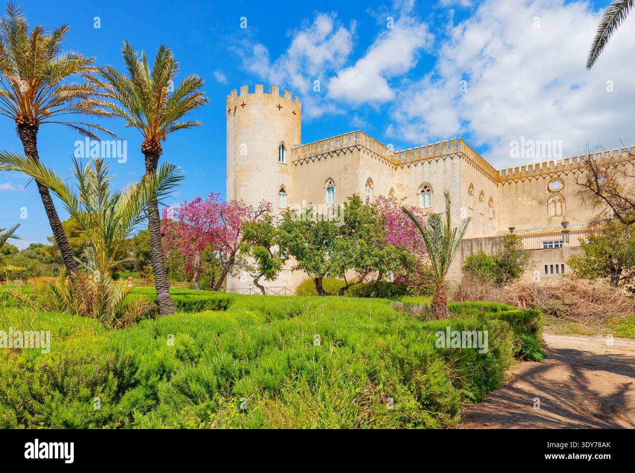 Besucher genießen die Gärten der Burg Donnafugata in Ragusa, Sizilien, unter einem hellblauen Himmel mit Palmen und bunten Blumen Stockfoto