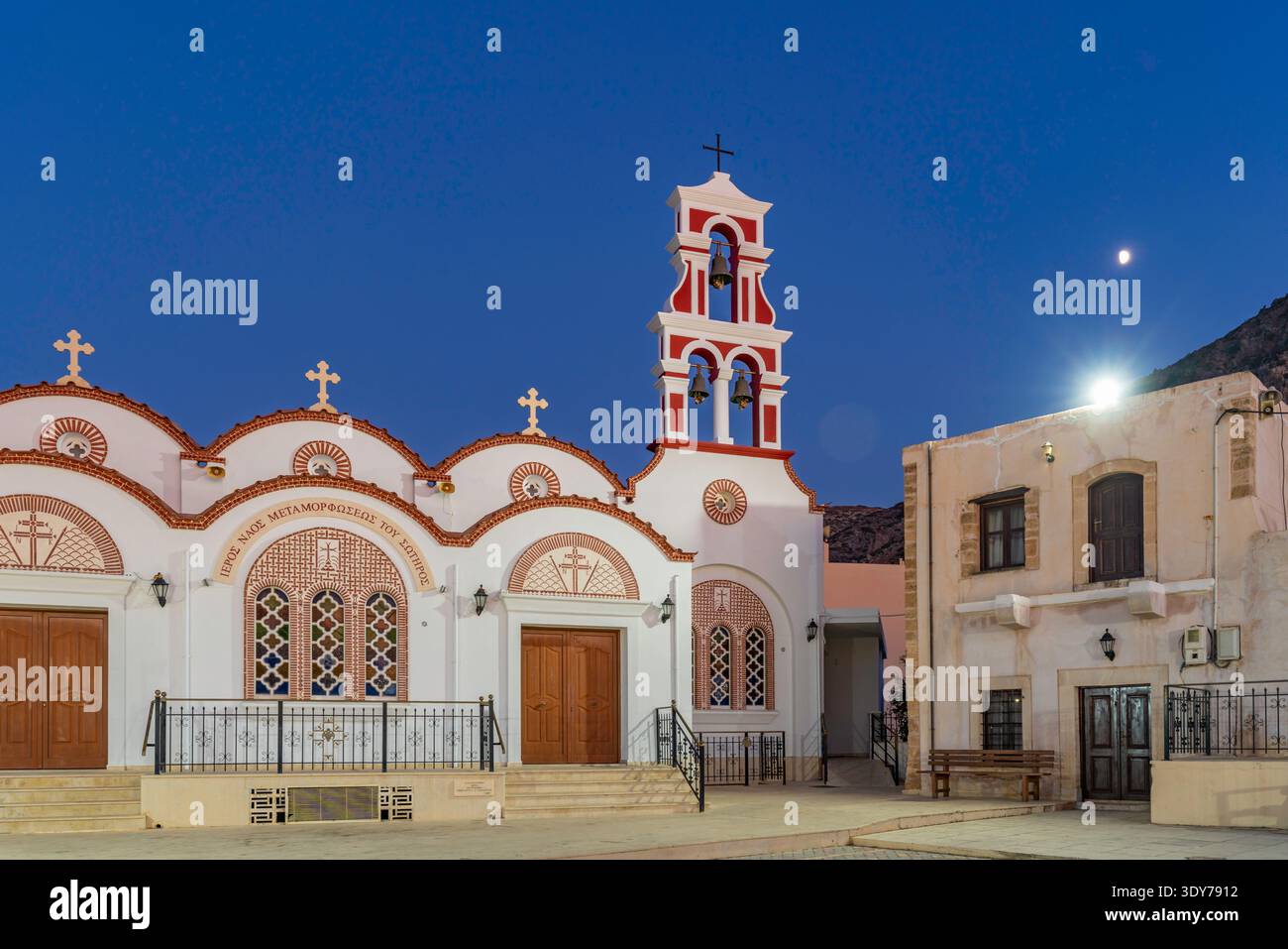 Blick auf die Kirche der Metamorphose des Erlösers im Dorf Piskopiano in der Abenddämmerung mit warmen Lichtern und Mond darüber Stockfoto