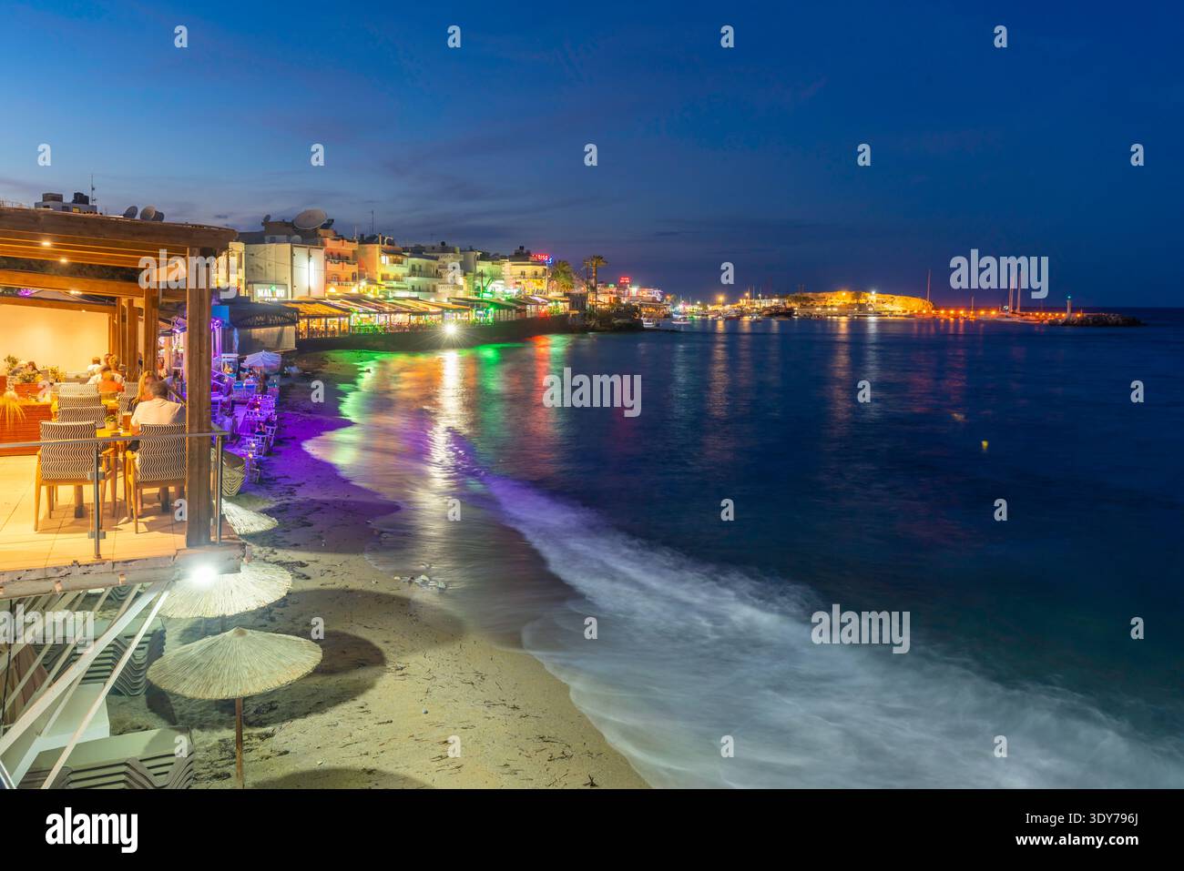 Blick in die Abenddämmerung auf den Strand von Limenas Chersonisou mit Stadtlichtern am Meer auf Kreta, Griechenland Stockfoto