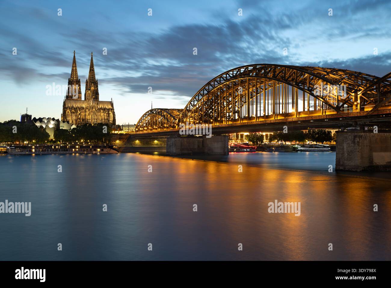Die Hohenzollernbrücke überspannt den Rhein mit dem bei Nacht beleuchteten Kölner Dom in Nordrhein-Westfalen Stockfoto