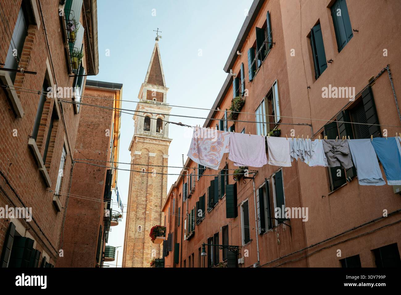 Waschen hängt an Schlangen in einer engen Straße in der Nähe eines Glockenturms in Castello, Venedig, unter klarem Himmel Stockfoto