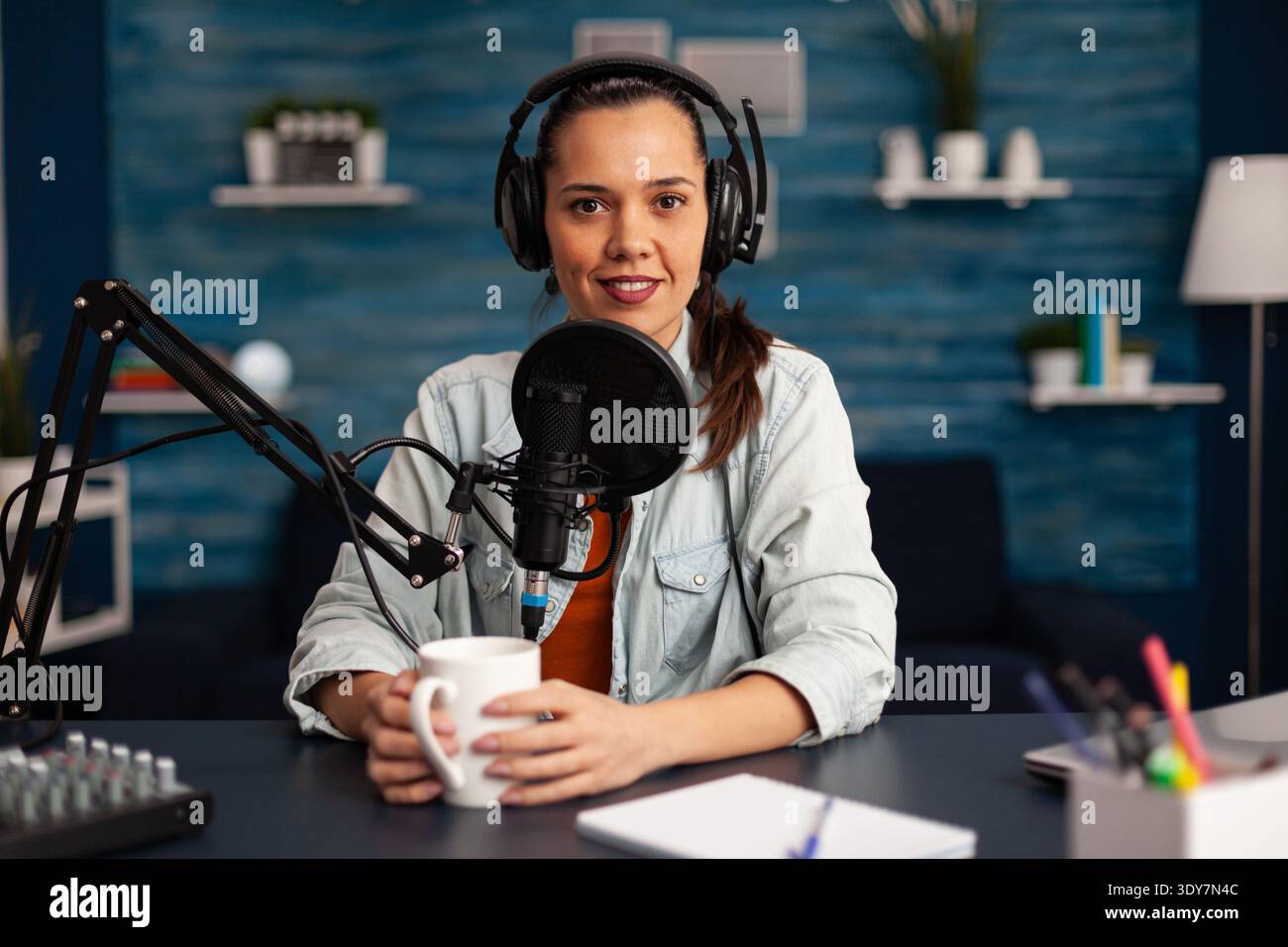 Vlogger sendet ihr Publikum, während sie im Heimstudio Podcasts für soziale Medien macht. Blogger, die Online-Talkshow mit Kopfhörern aufnehmen, professionelles Mikrofon, das während der Übertragung auf die Kamera blickt. Stockfoto