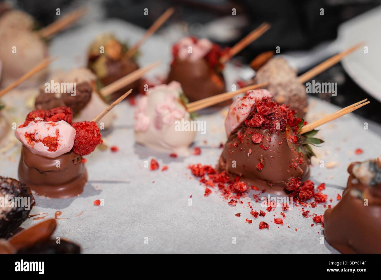 Nahaufnahme von handgefertigten Erdbeeren mit Schokoladenüberzug, verziert mit verschiedenen Belägen und Streuseln auf Backpapier. Gourmet-Dessert-Konzept, Konfekt Stockfoto