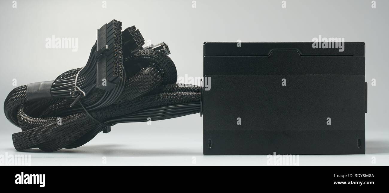 Schwarzes Computer-Netzteil isoliert neutraler grauer Hintergrund, gebündelte geflochtene Kabel und Anschlüsse für netzteil, Modell-Vorlage, Seitenansicht Stockfoto