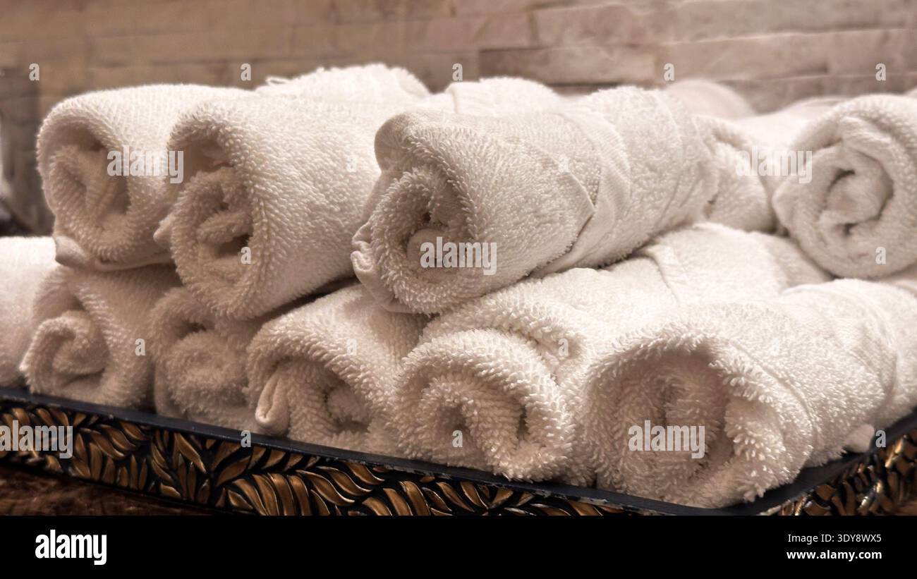 Ein Stapel weicher, weißer Handtücher, zusammengerollt und ordentlich in einer luxuriösen Umgebung angeordnet, perfekt für High-End-Hotels, Spas oder elegante Badezimmer. Stockfoto