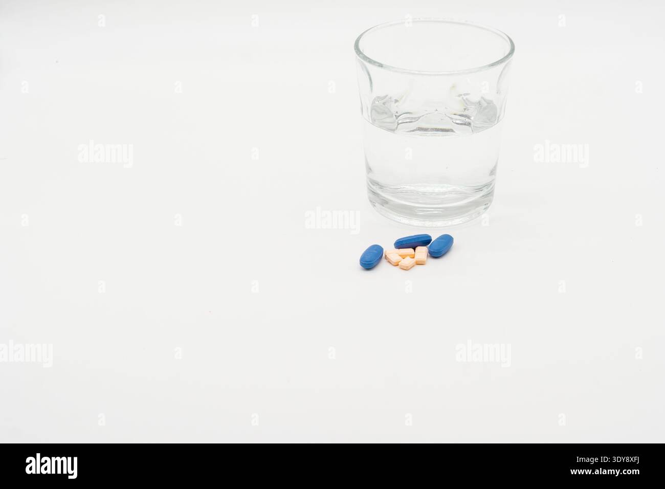 Glas Wasser mit mehreren Pillen auf einer weißen Oberfläche, minimales sauberes Stillleben. Stockfoto