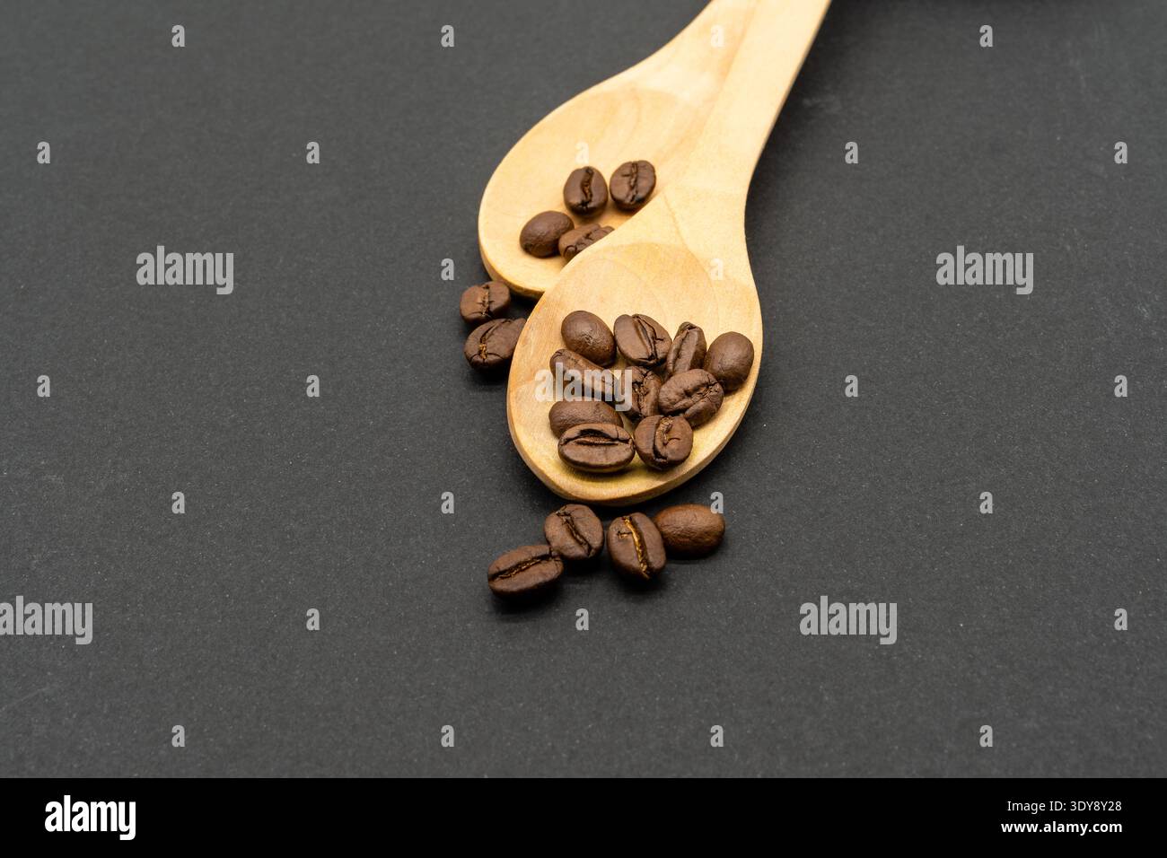Zwei Holzlöffel mit mittelgerösteten Kaffeebohnen auf dunklem, strukturiertem Hintergrund Stockfoto