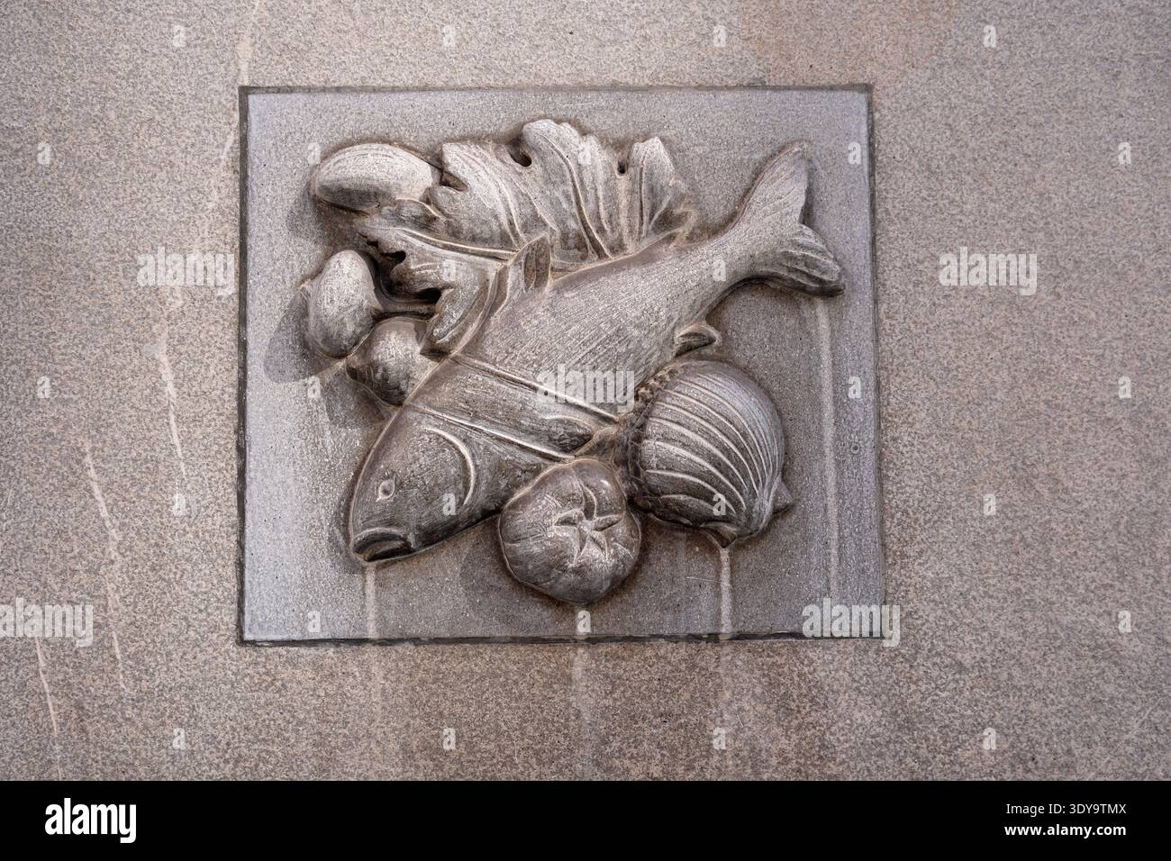 Eine Steinreliefschnitzerei mit einem Fisch, begleitet von einer Muschel und Gemüse an der Wand eines Ladens in Wien Austira Stockfoto