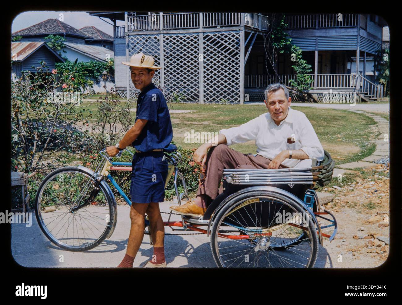 Ein amerikanischer Tourist, der von einem lokalen Fahrer eine Fahrradtour mit dem Pedicab und der Rikscha bekommt. Diese Folie, Kodachrome, wurde von einem amerikanischen Paar auf einer Reise nach Bangkok, Siam, Thailand im Jahr 1954 aufgenommen. Die Farbe auf dem Foto ist lebendig, fast handgetönt, bemalt. Stockfoto