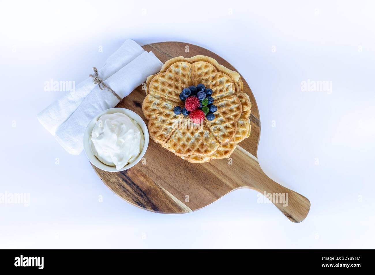 Schwedische Waffeln in Herzform mit frischen Heidelbeeren, Himbeeren und Schlagsahne auf einem Holzbrett Stockfoto